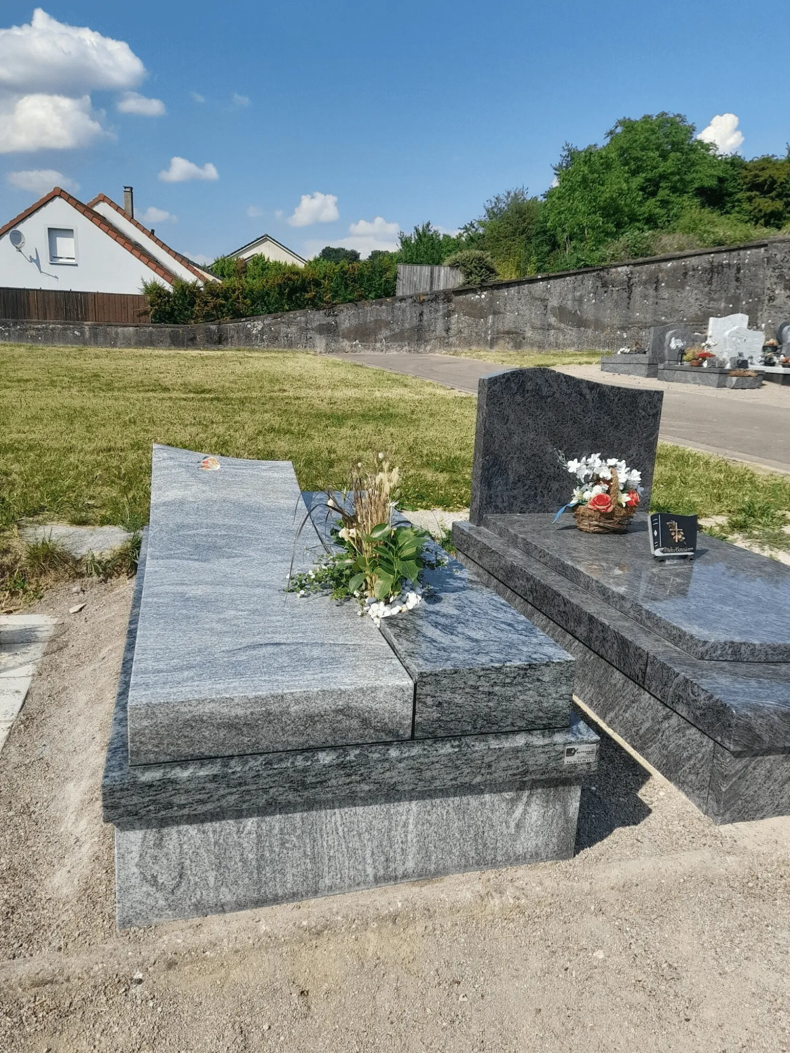 Monument funéraire en granit gris clair avec pierre tombale inclinée décorée de fleurs