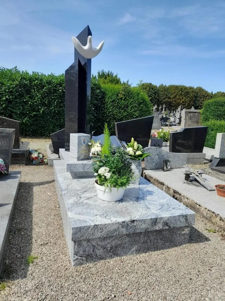 Sépulture moderne en granit clair décorée d'une composition végétale au cimetière